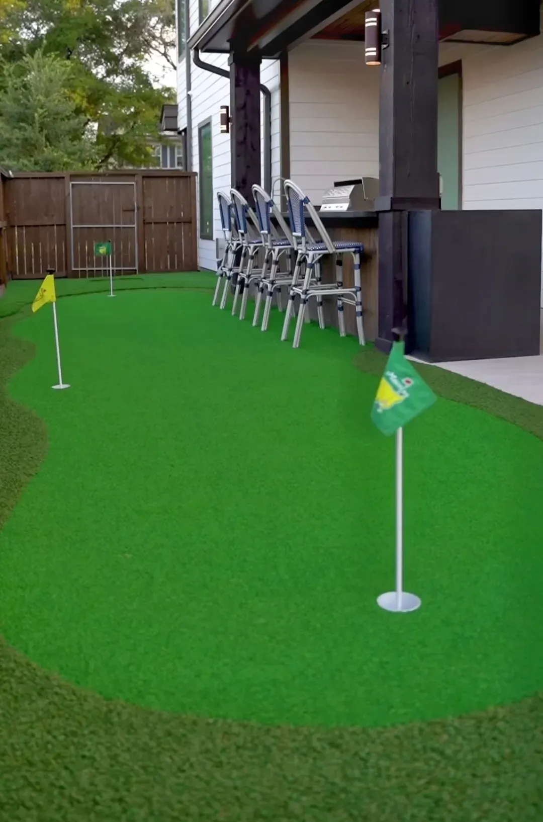 The covered-patio green from the garden, bar stools along the outdoor kitchen
