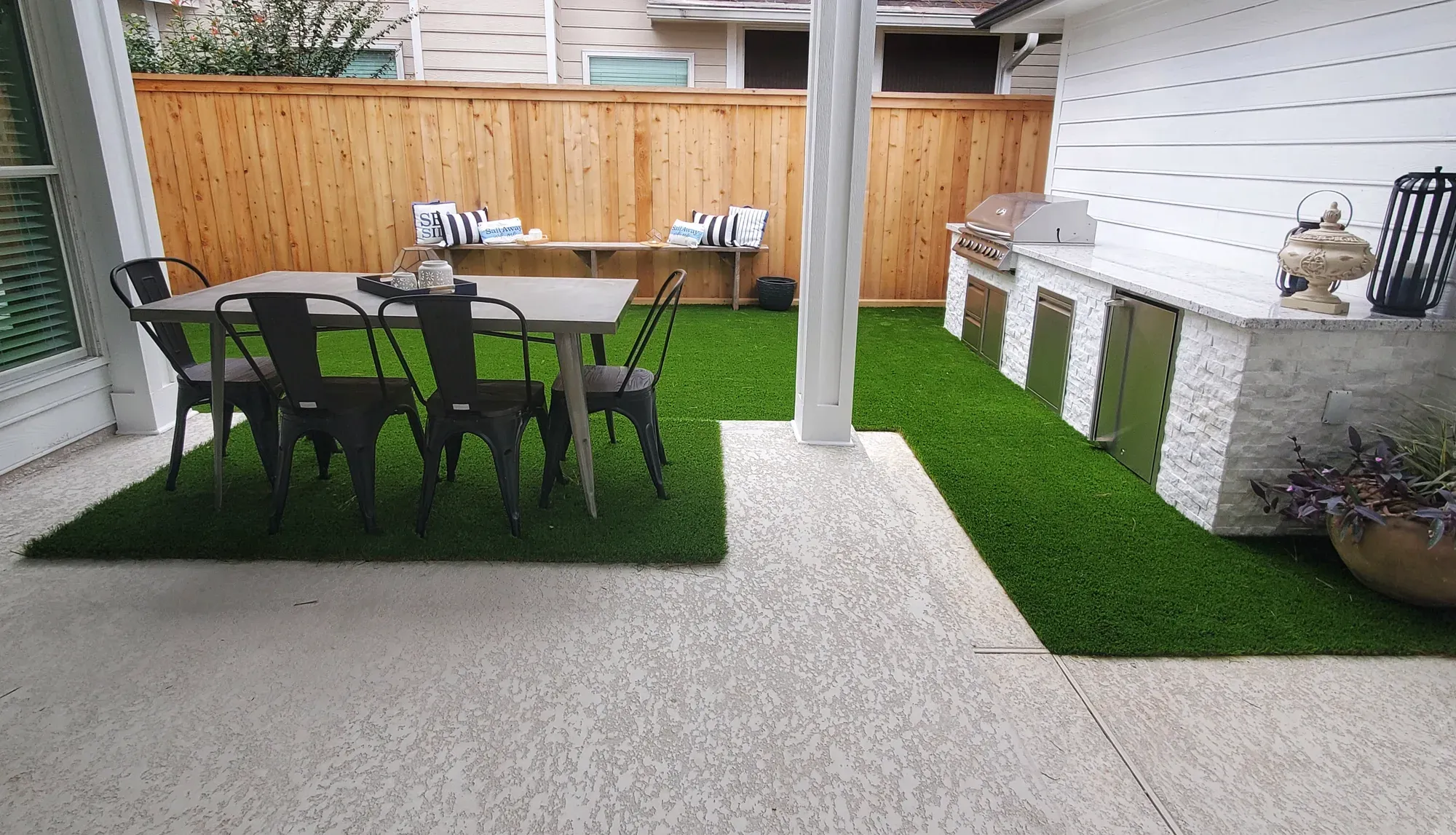 Artificial turf laid in panels within a concrete patio, one panel under a dining table and chairs and another running beside an outdoor kitchen