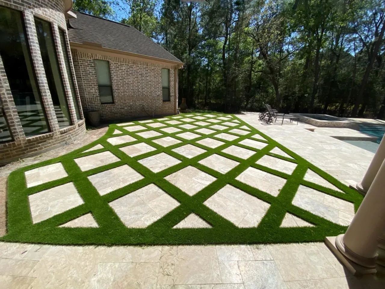 A patio set out as a diamond lattice of travertine paving with artificial turf strips between