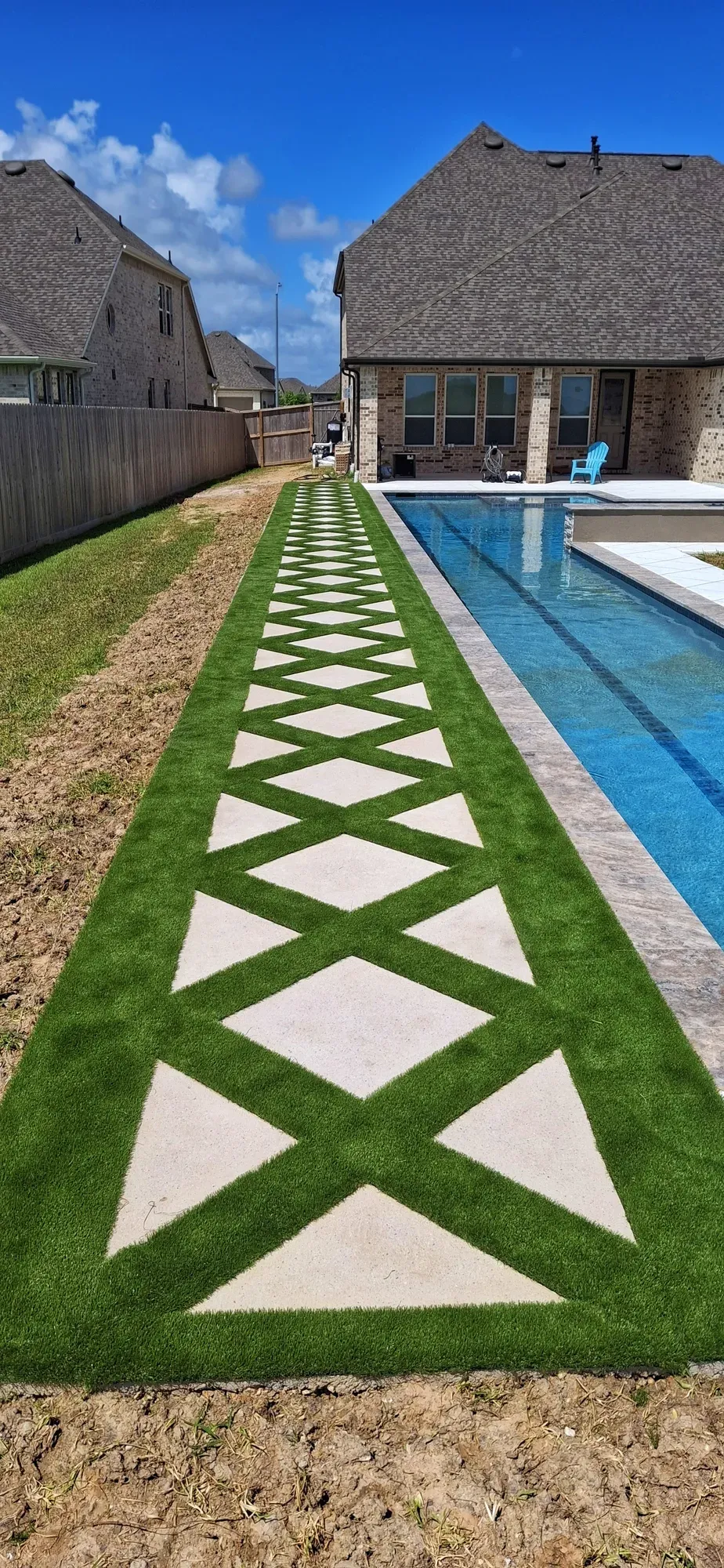 A long diamond-patterned paver-and-turf strip beside a pool