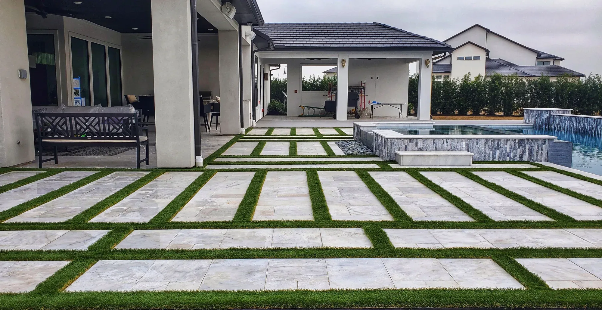 A grid of pale pavers with green turf joints running the length of a pool deck