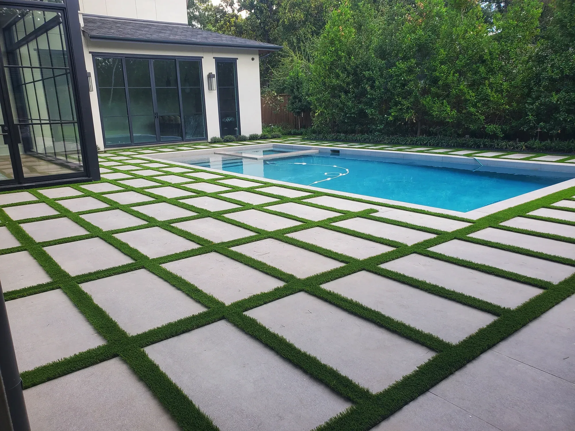 A grid of pale pavers with turf joints around a rectangular pool