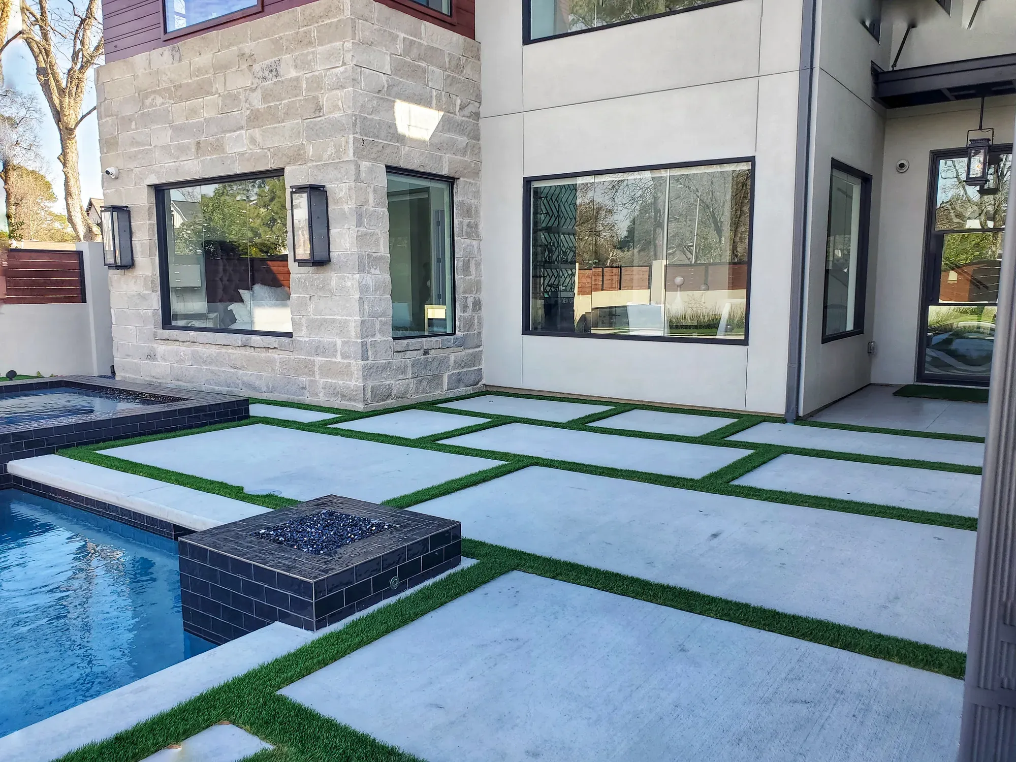A large-format paver terrace with turf joints wrapping a pool and a square fire feature