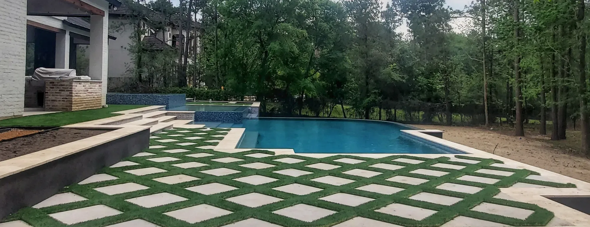 A long pool with a broad grid of pavers and turf joints on the deck