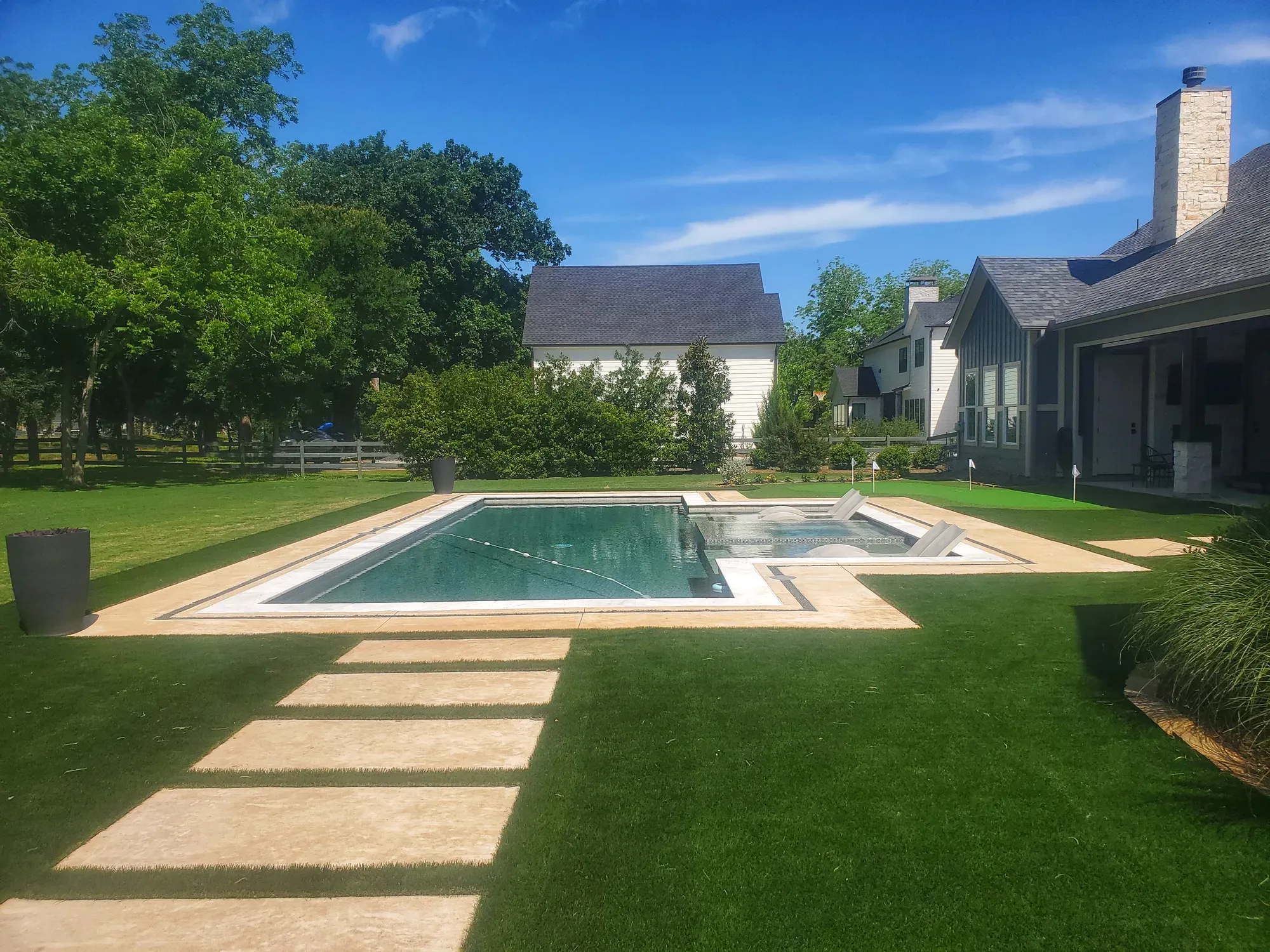 A pool and paved terrace with turf strips and a turf lawn beyond