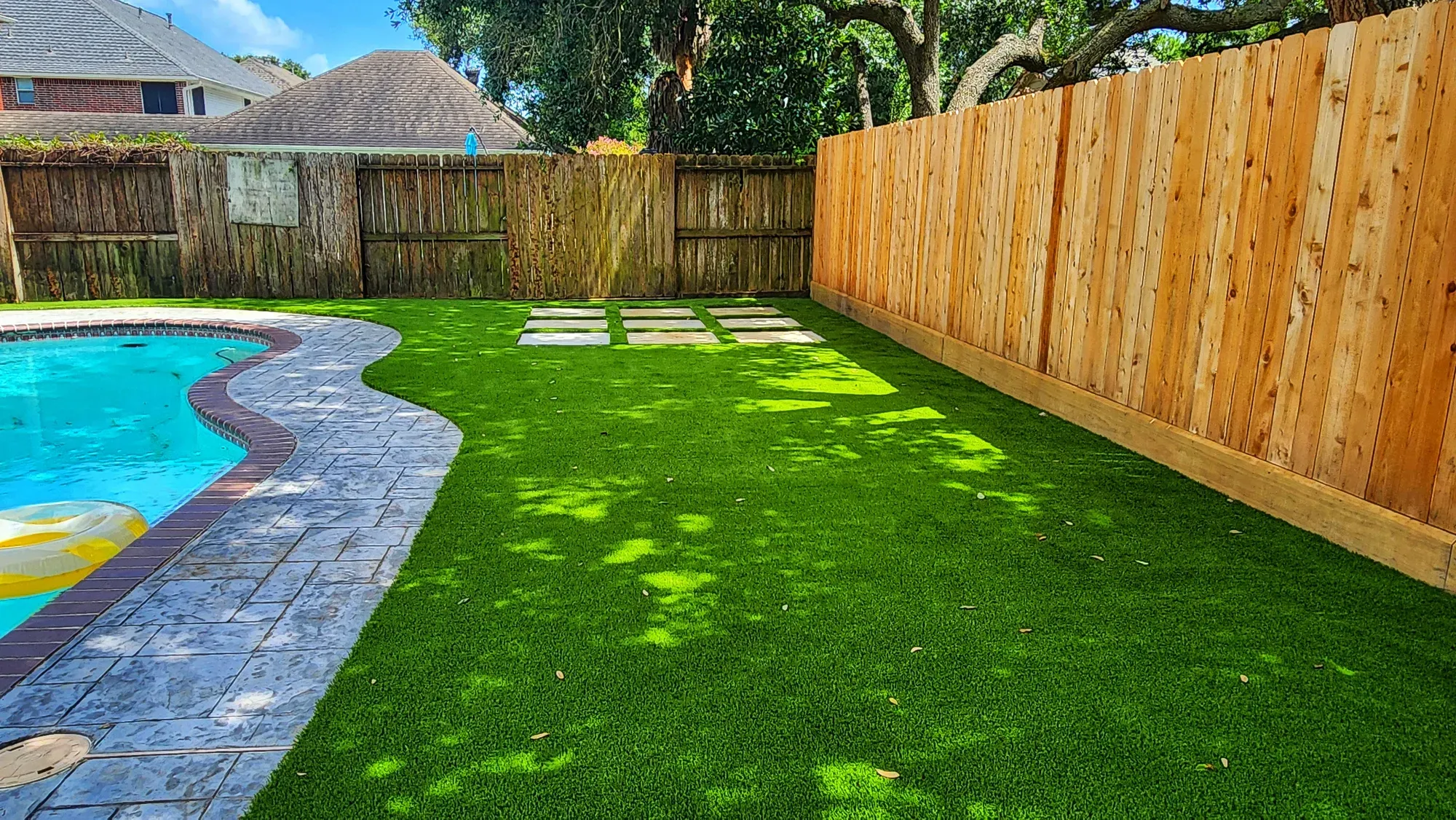 An artificial turf lawn running along a pool to a timber fence