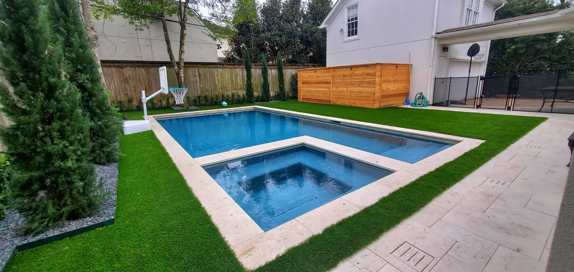 A rectangular pool with artificial turf around it and a timber screen behind