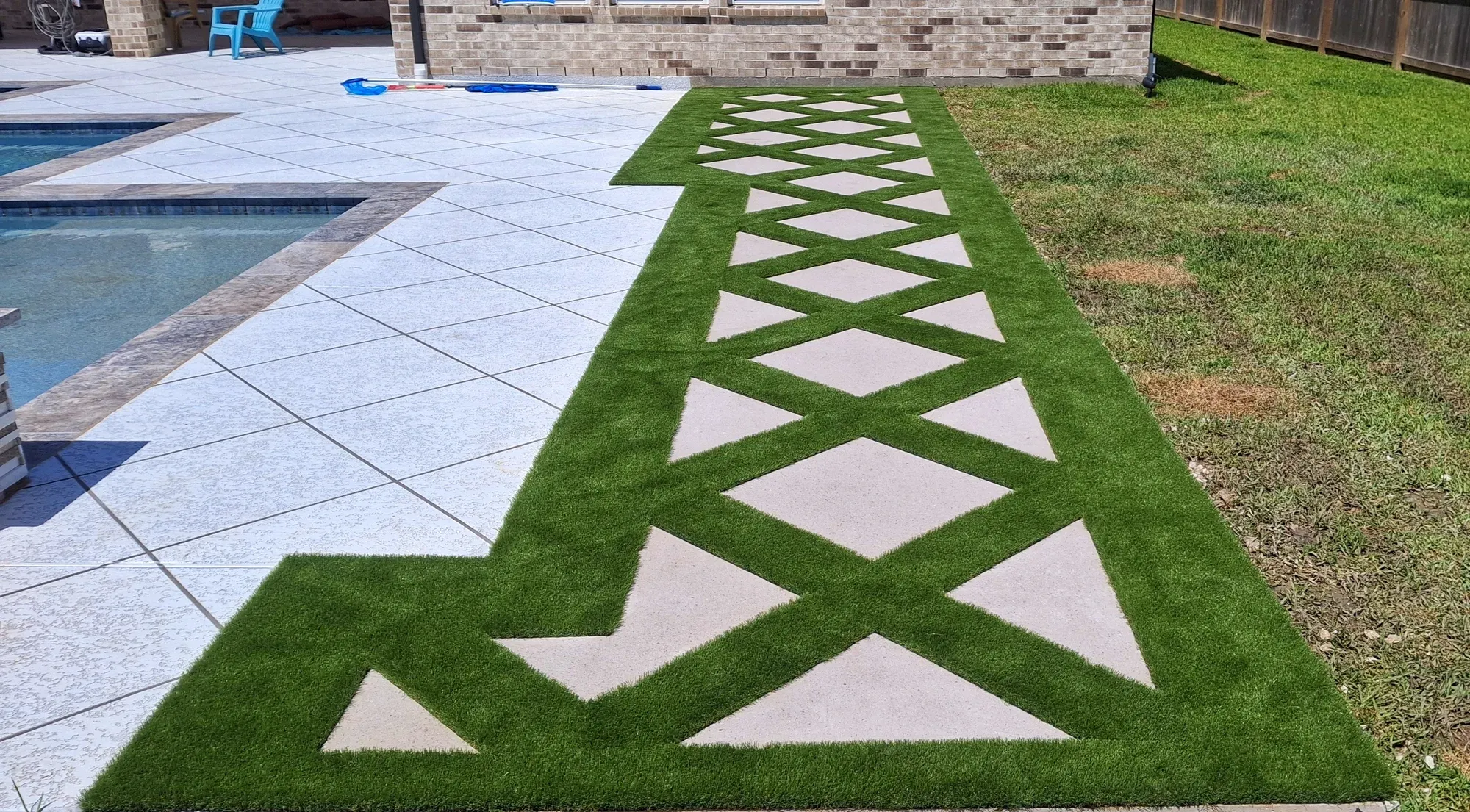 A diamond lattice of pavers and turf running between a pool deck and the fence