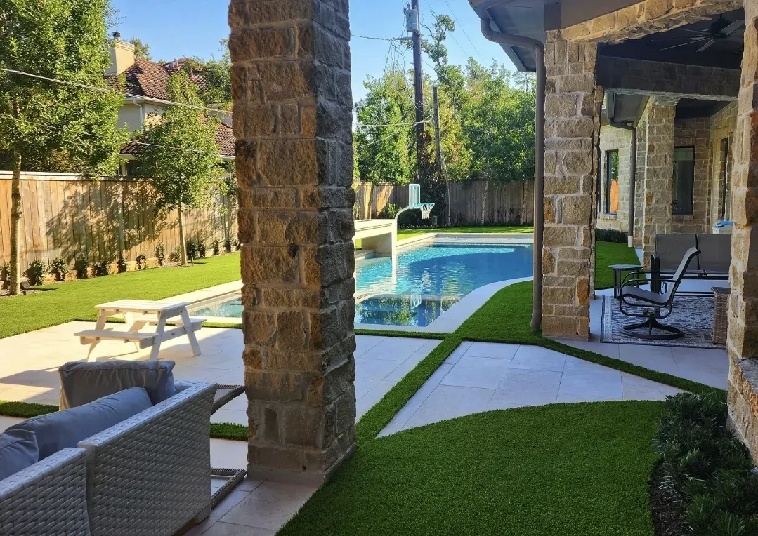 A pool and covered patio seen past stone columns, with artificial turf between
