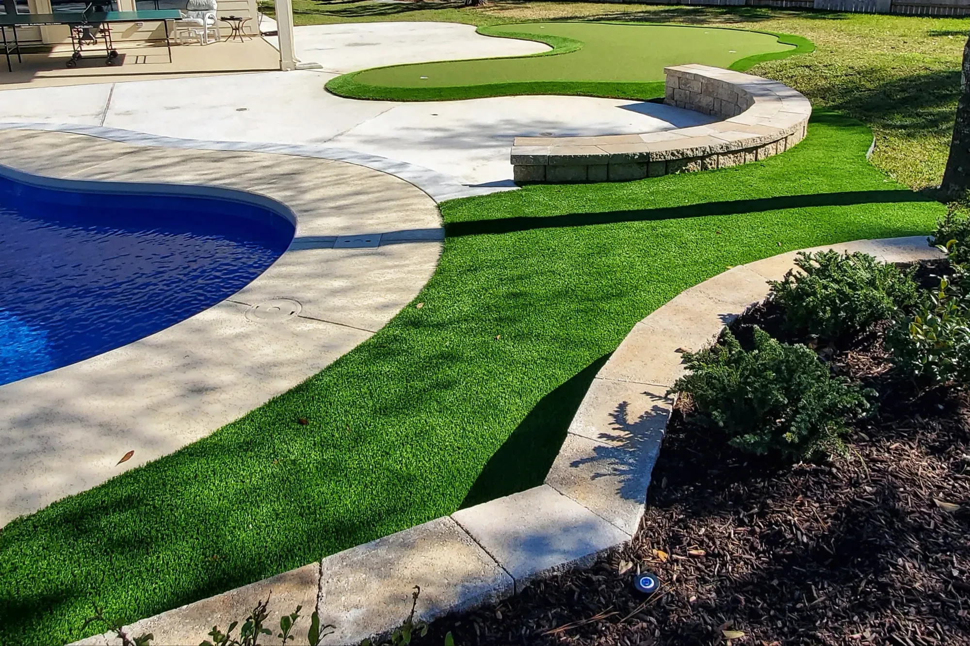 A curved practice green and turf lawn wrapping a blue swimming pool