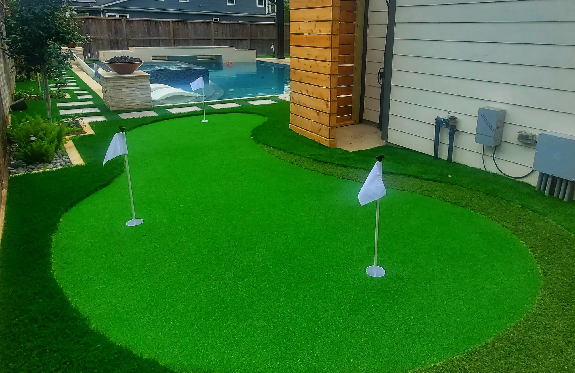 A small practice green with a flag beside the pool and a timber screen
