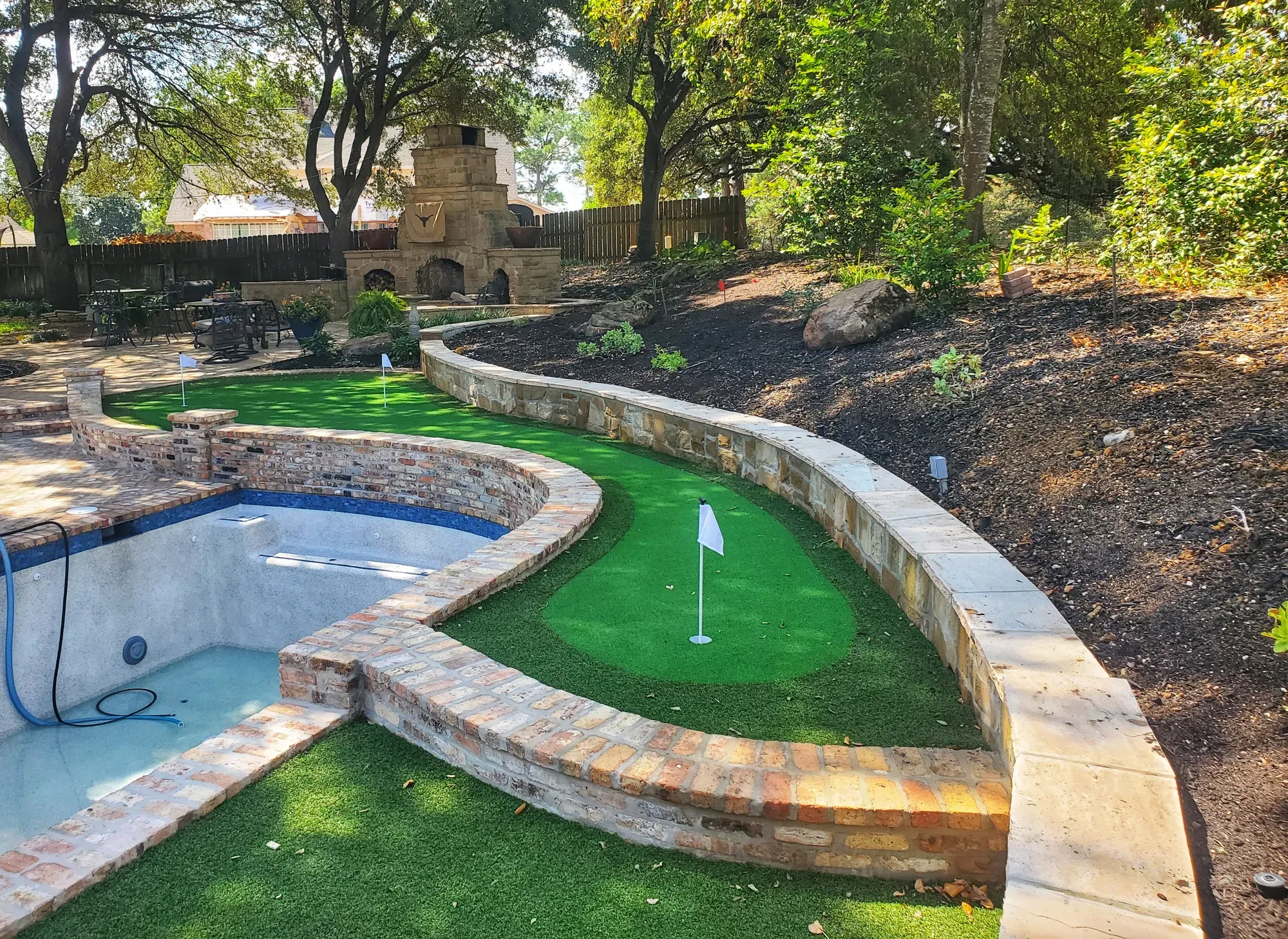 A backyard pool with a small artificial putting green alongside it, edged in stone