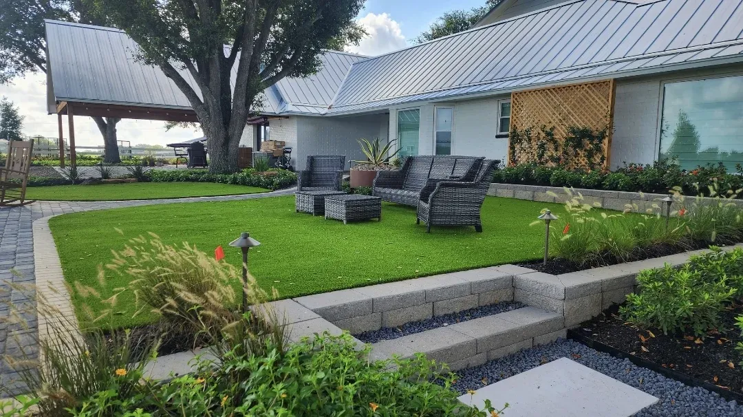 Grey loungers on a paved terrace beside an artificial lawn and a low retaining wall