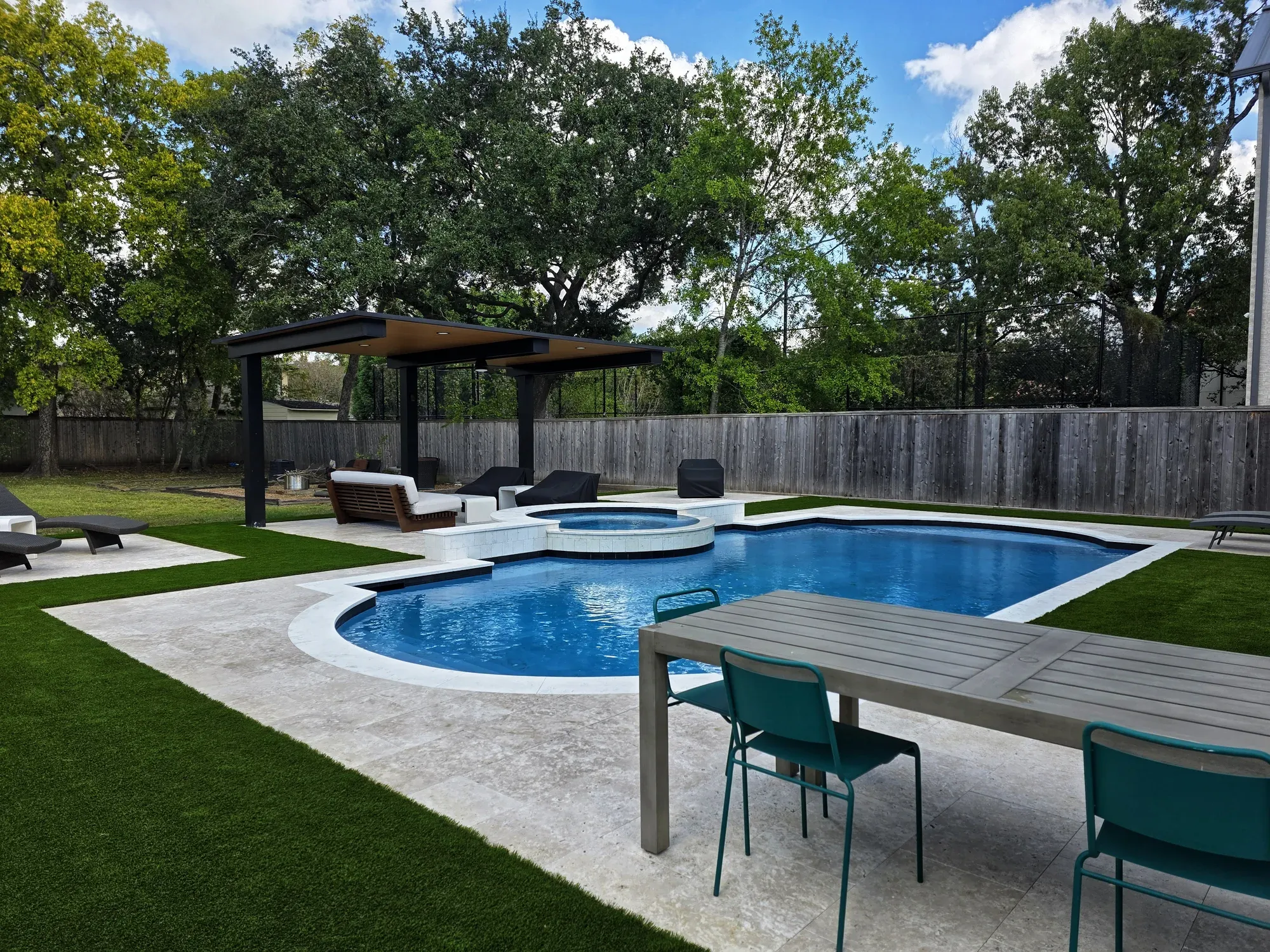 A pool and pergola with artificial turf between the deck and the fence