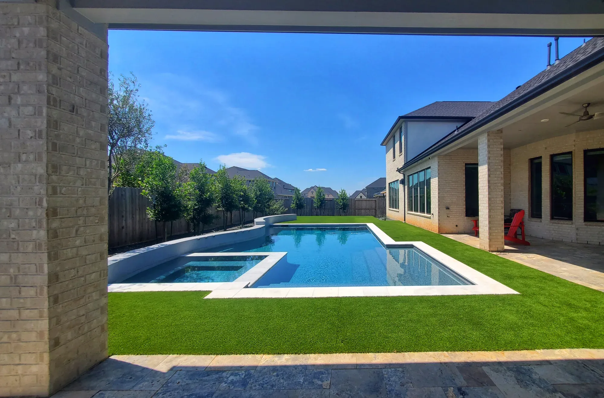 An artificial turf lawn running alongside a long rectangular pool, seen from a covered patio