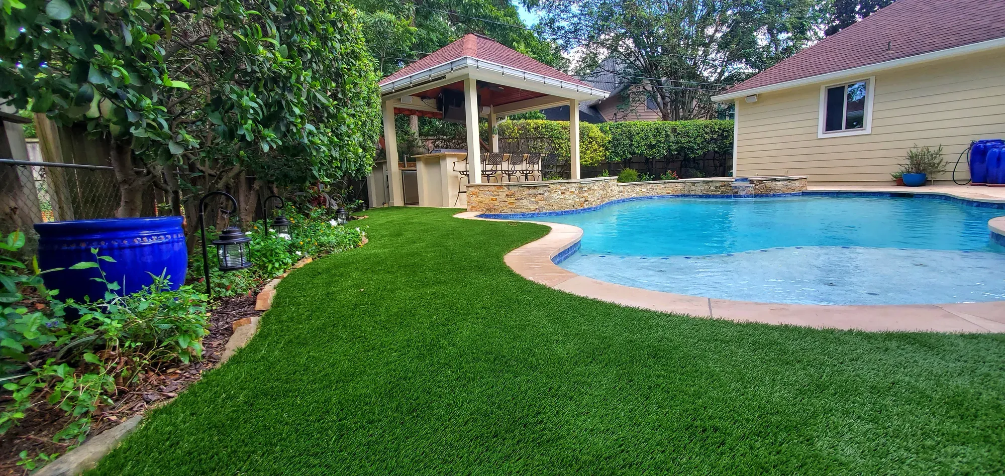 An artificial turf lawn wrapping a freeform pool with a covered cabana behind