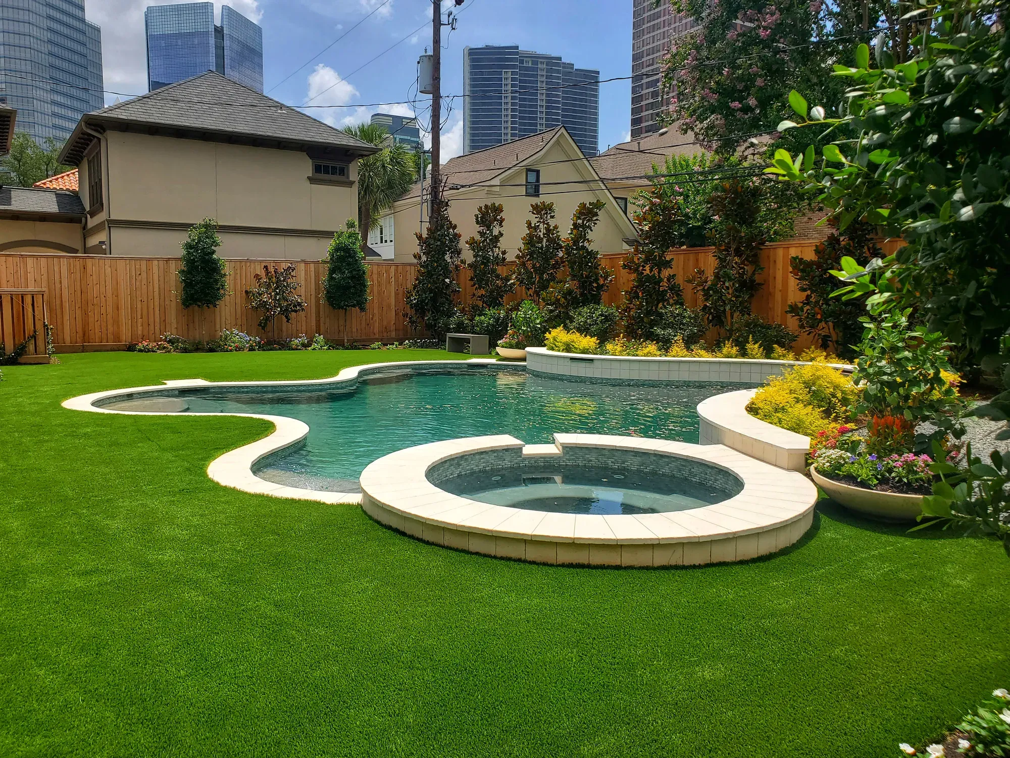 A curved pool and spa set into an artificial turf lawn in a fenced yard