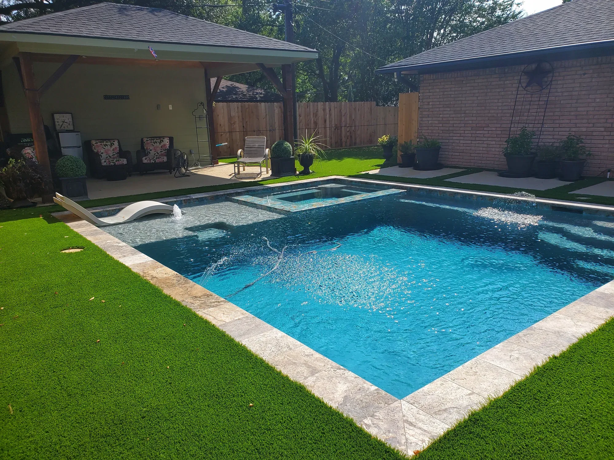 A rectangular pool with an artificial turf border and a covered patio beyond