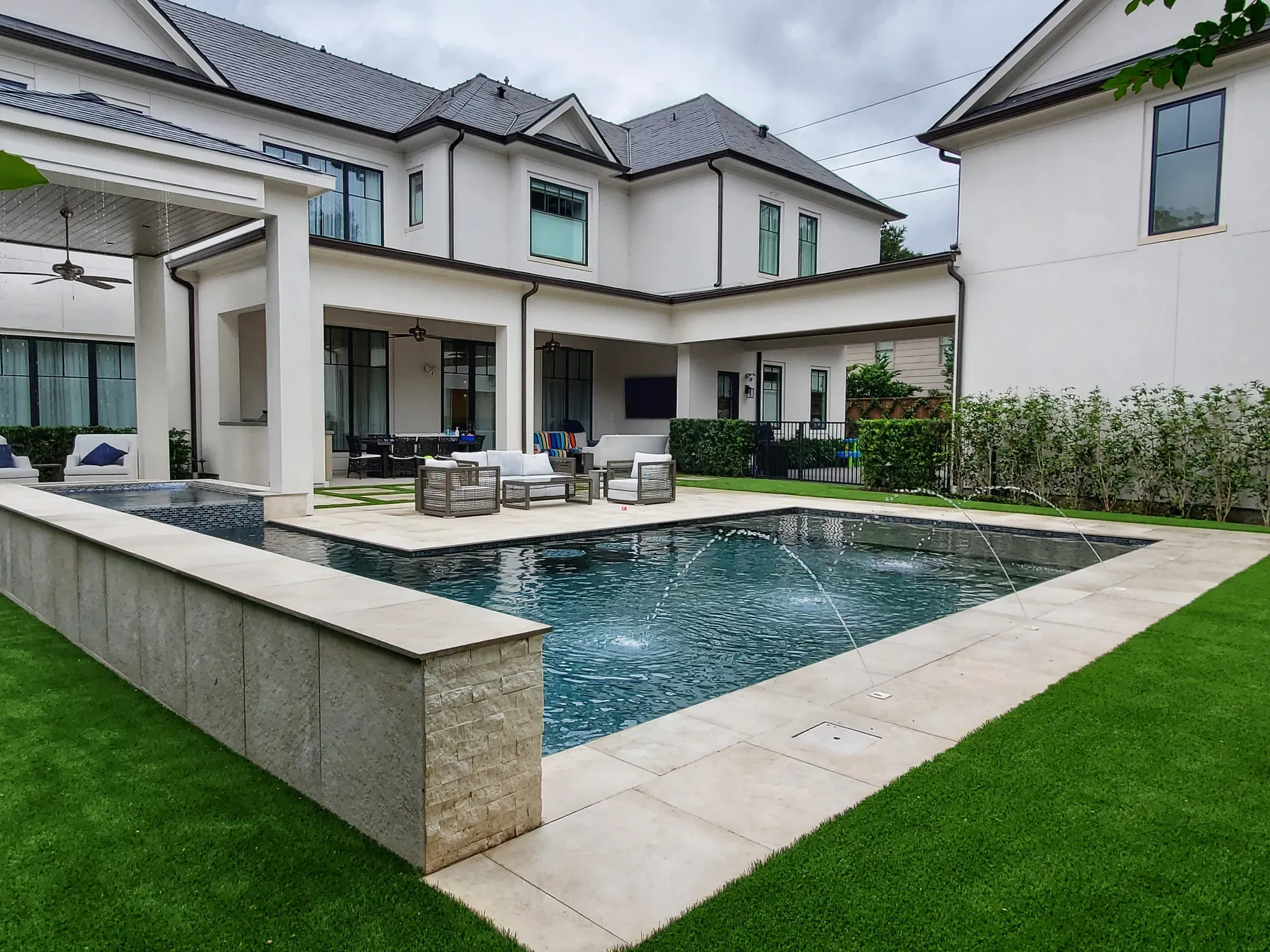 An artificial turf lawn wrapping a rectangular pool behind a two-storey home