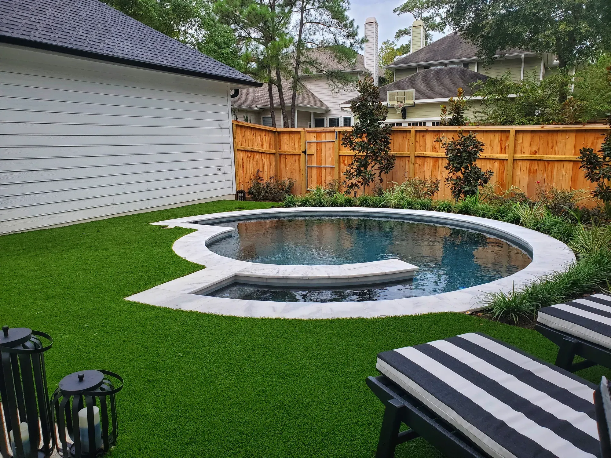 A circular pool set into an artificial turf lawn, with striped loungers on the grass