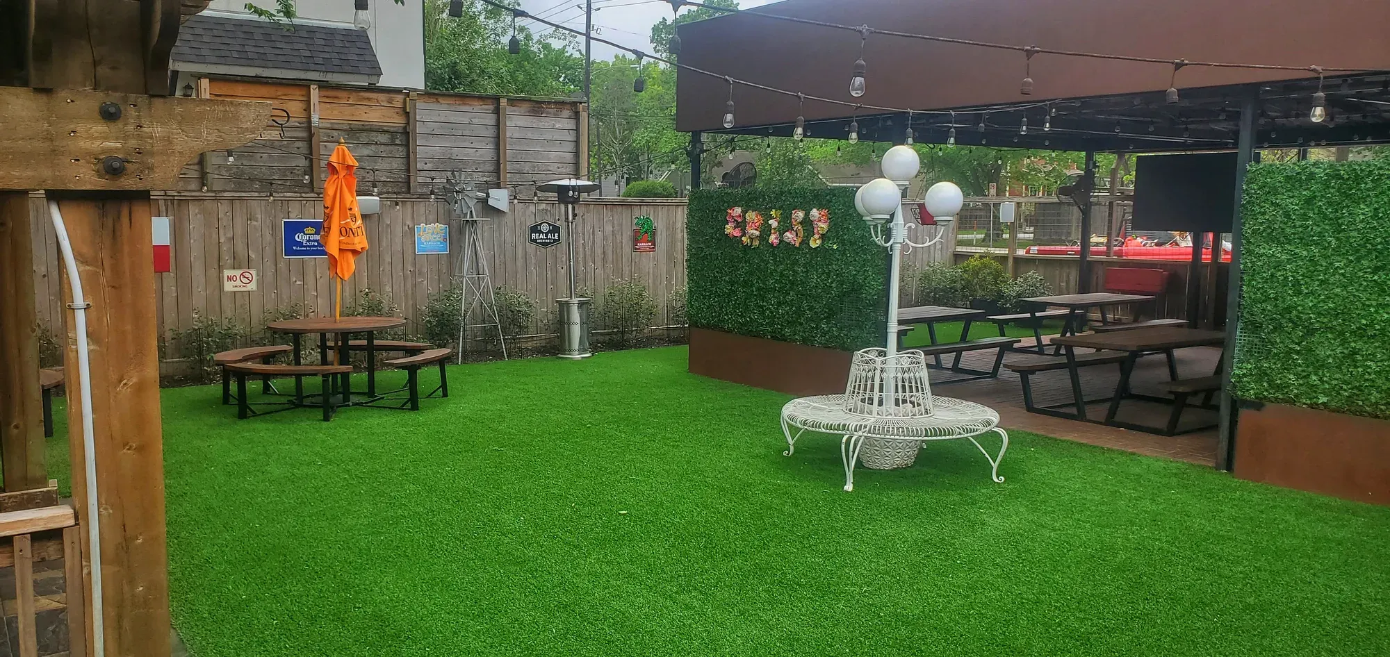Restaurant patio floored in artificial turf, with picnic tables, a boxwood screen wall and string lights strung overhead