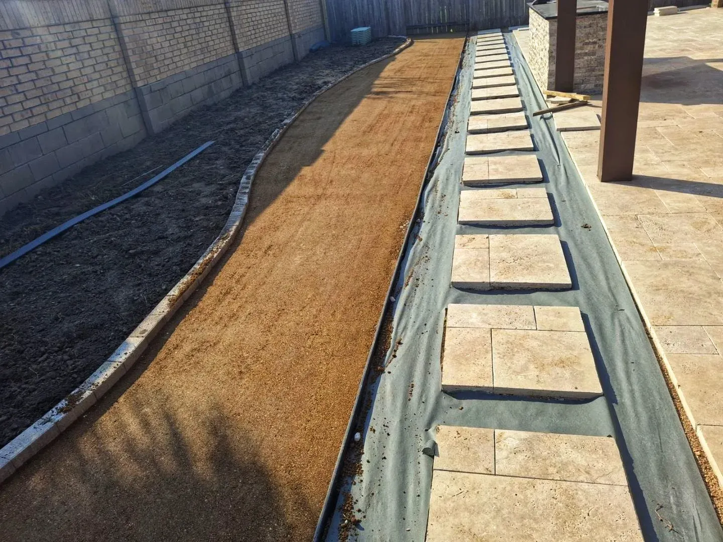 Compacted base and a screed rail run along the fence line before the turf goes down