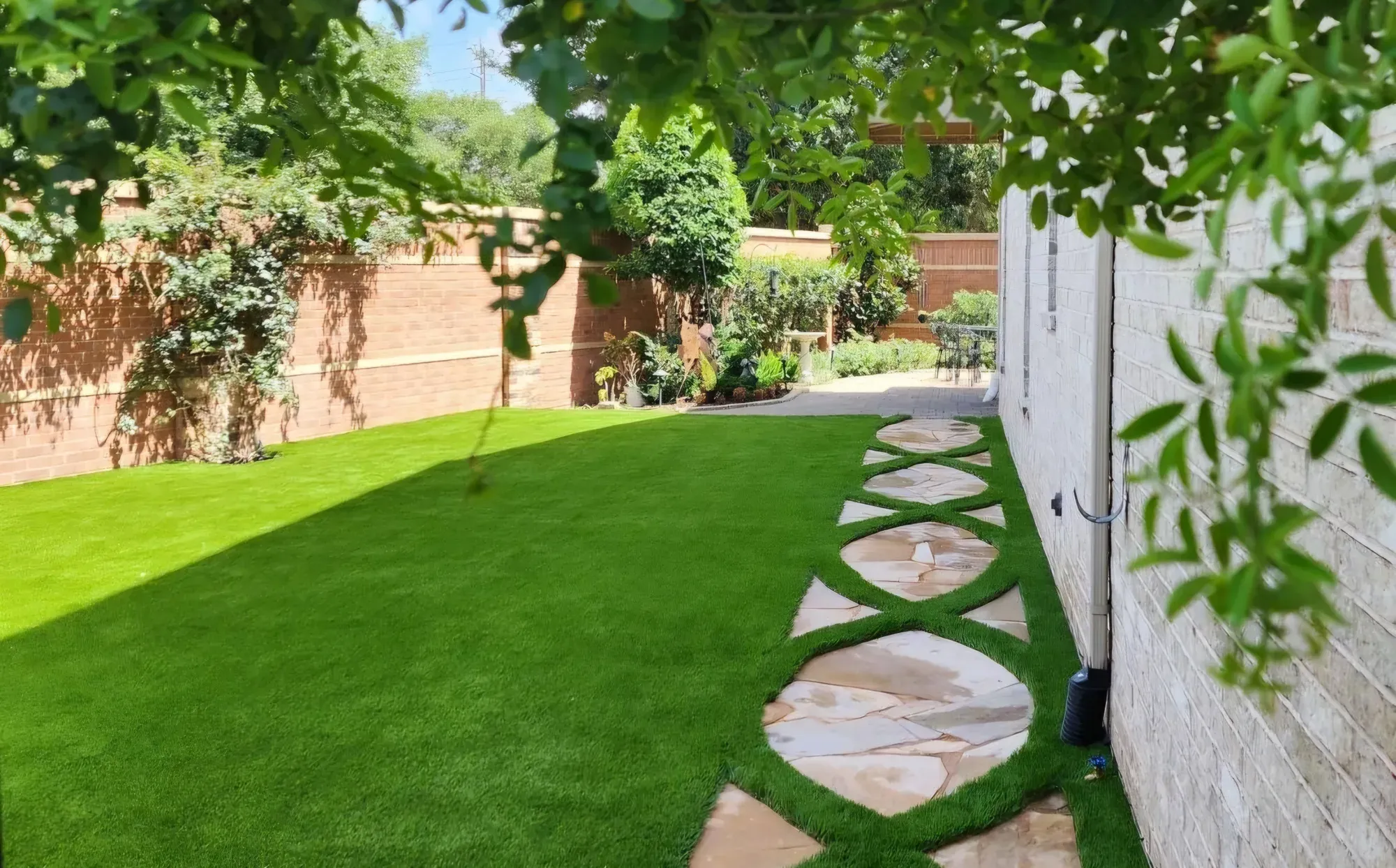 A path of circular stone steps set into artificial turf alongside a white rendered wall