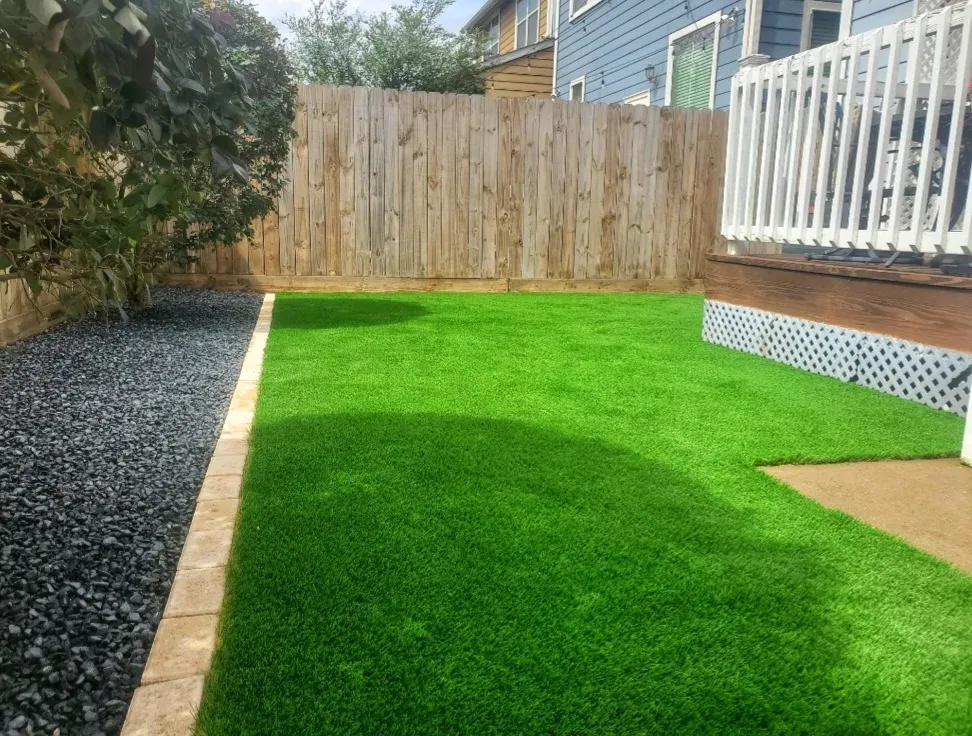 A small back lawn of artificial turf with a gravel border, timber fence and white deck rail
