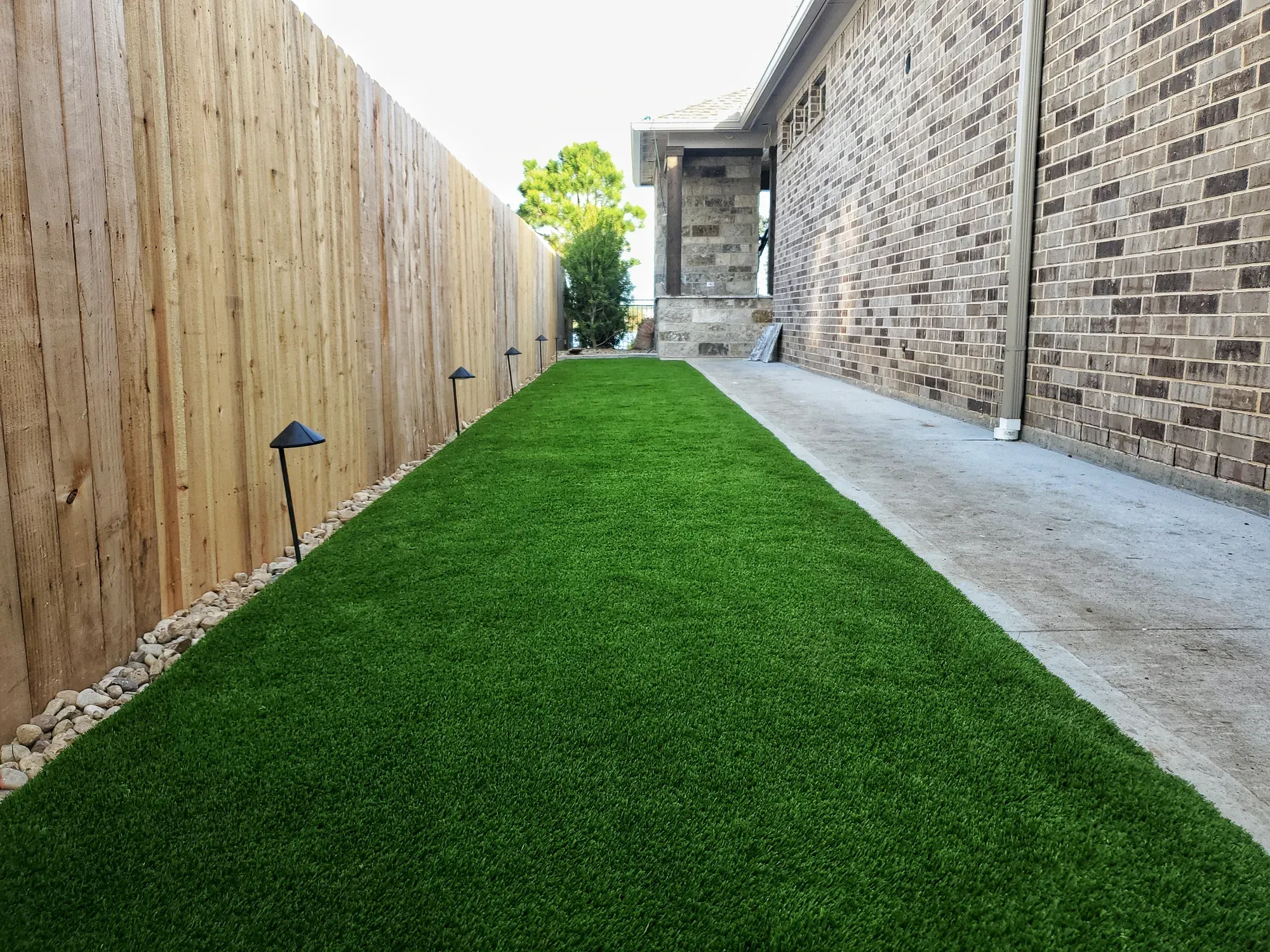 A narrow side yard laid in artificial turf between the house and the fence