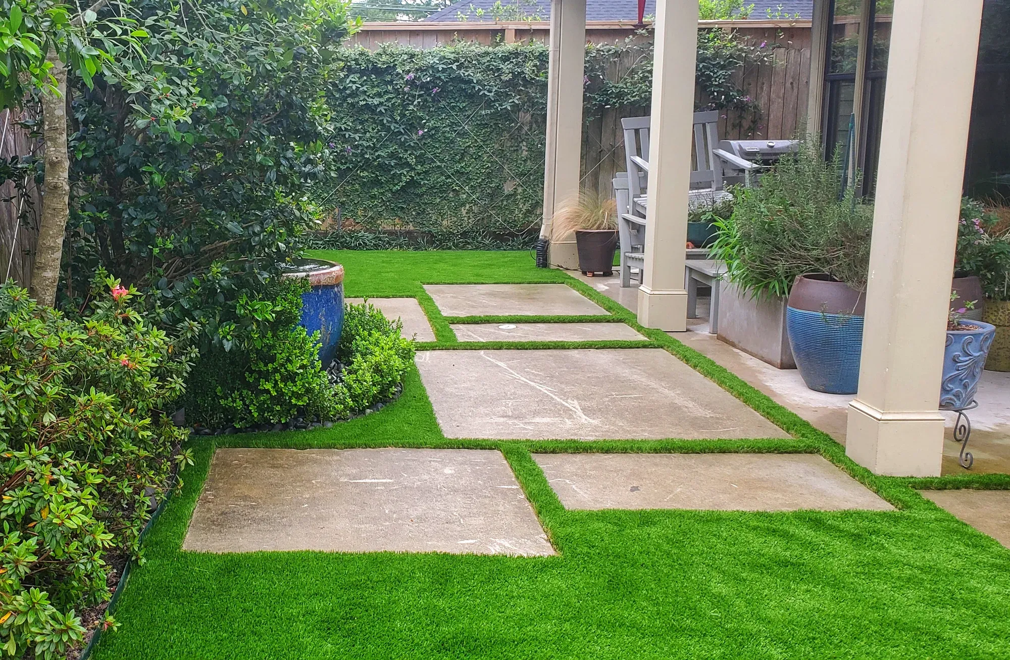 Large stone pavers set into artificial turf, forming a walkway between clipped hedging and planting beds