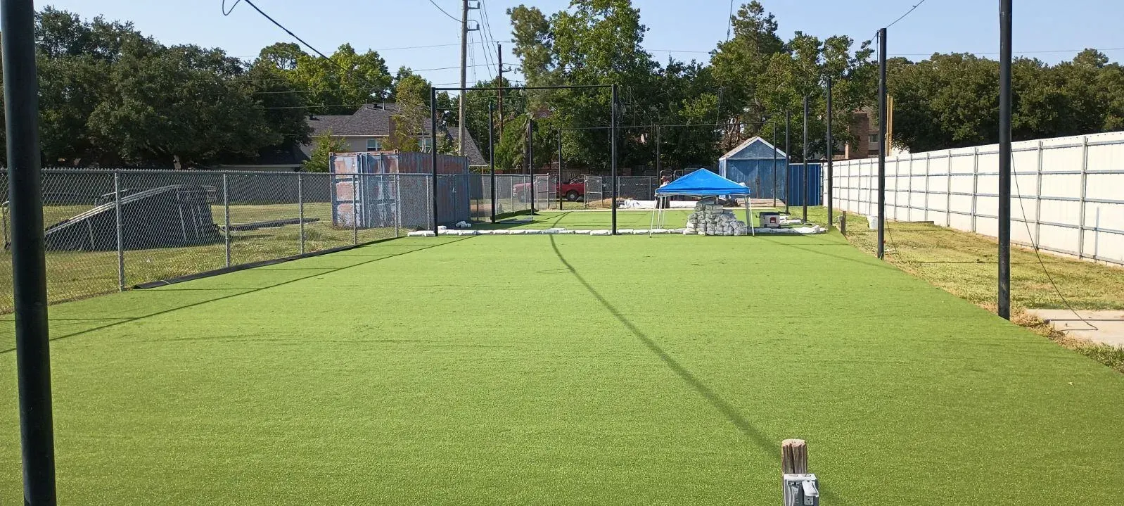 A long, straight run of artificial turf between two fence lines, running away from the camera