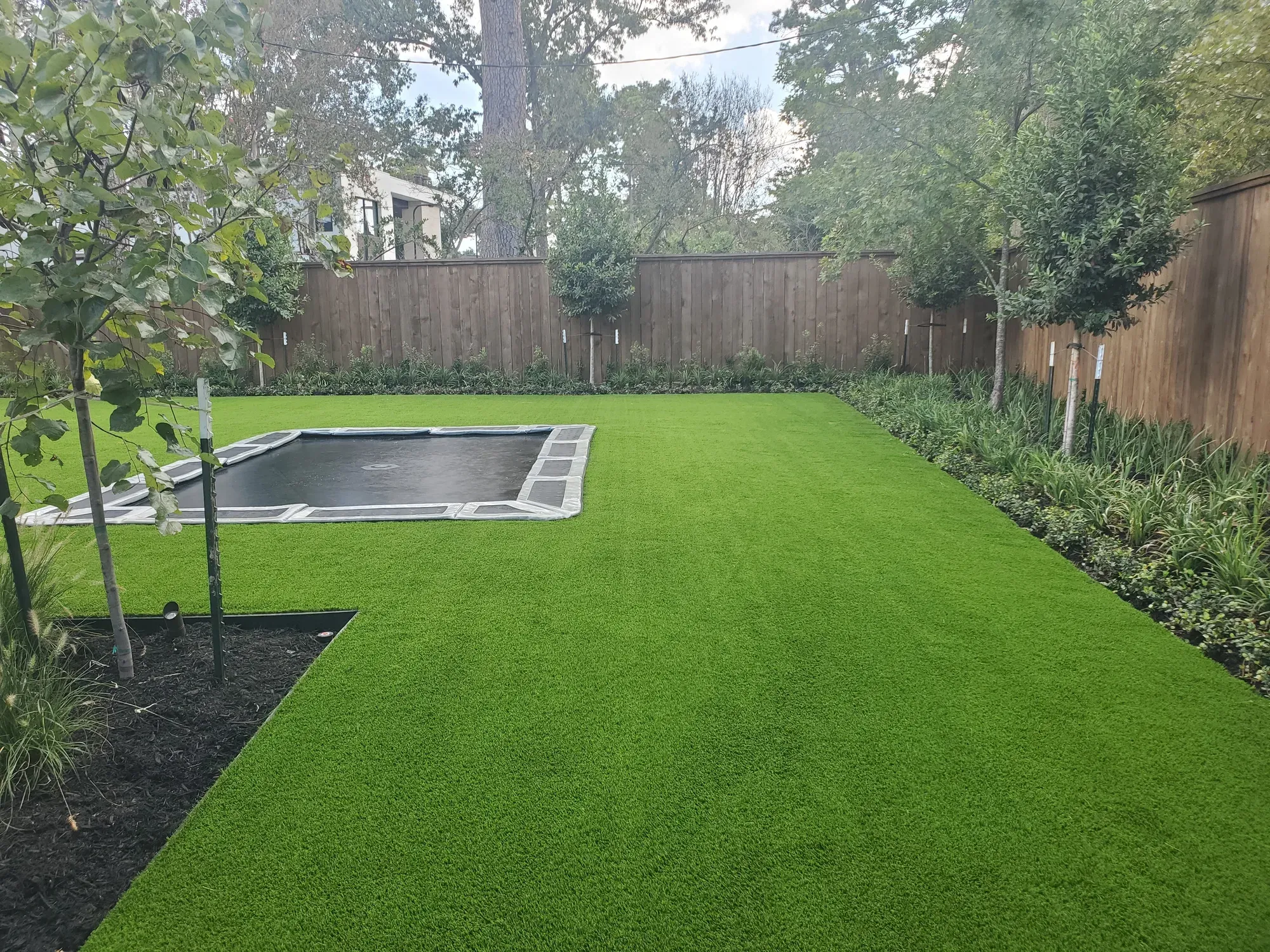 A wide artificial turf lawn with an in-ground trampoline set flush into it