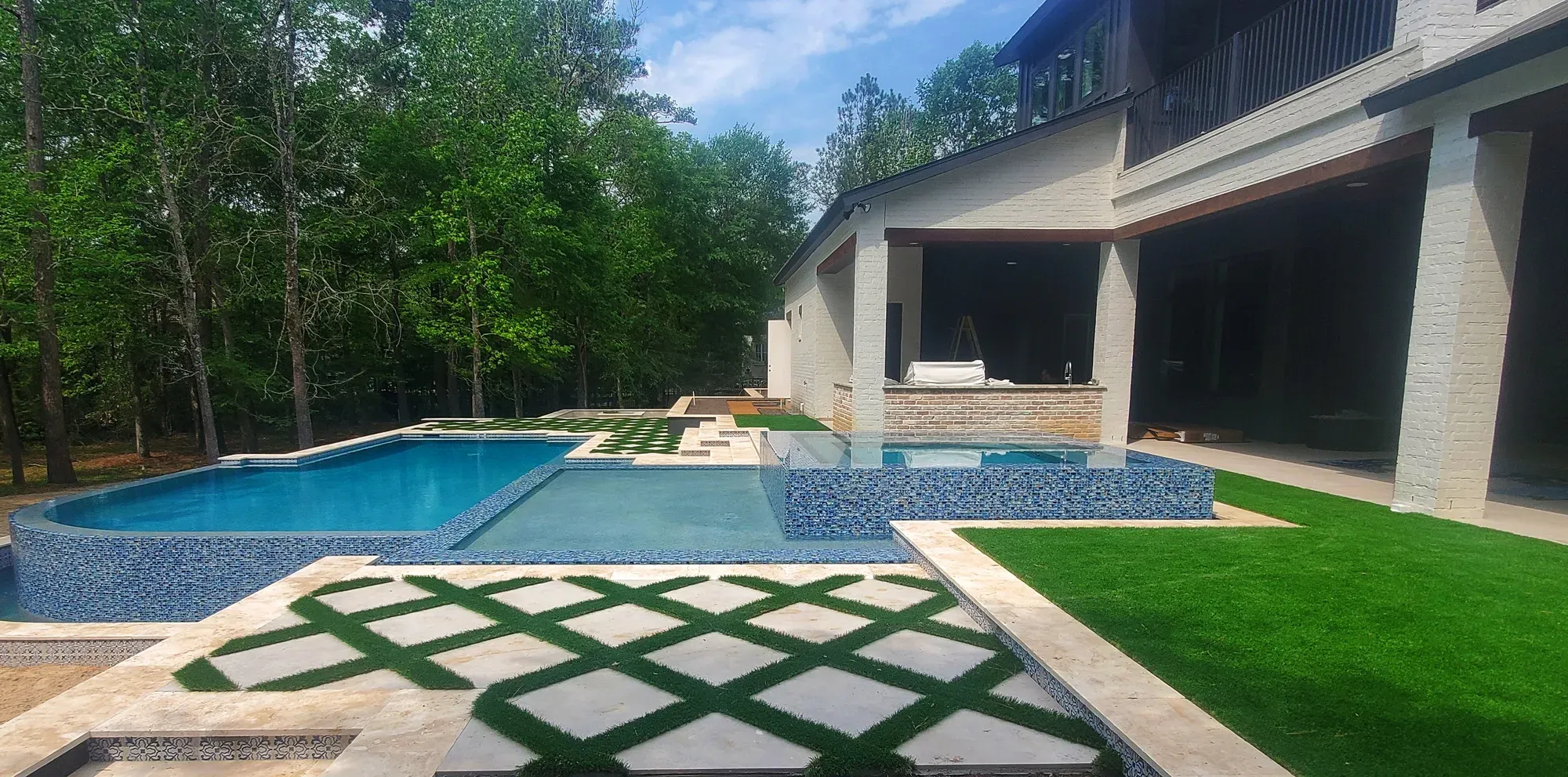 A modern pool and spa with paver-and-turf strips across the surrounding deck