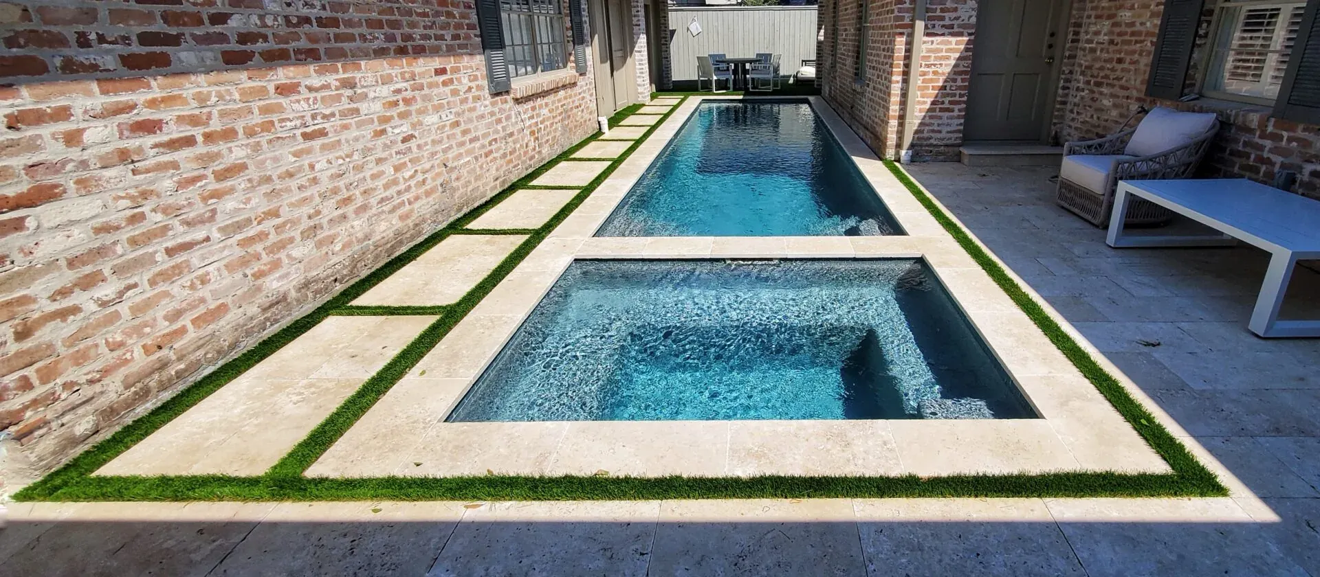 A narrow lap pool and spa in a brick courtyard, reached by turf-jointed stone steps