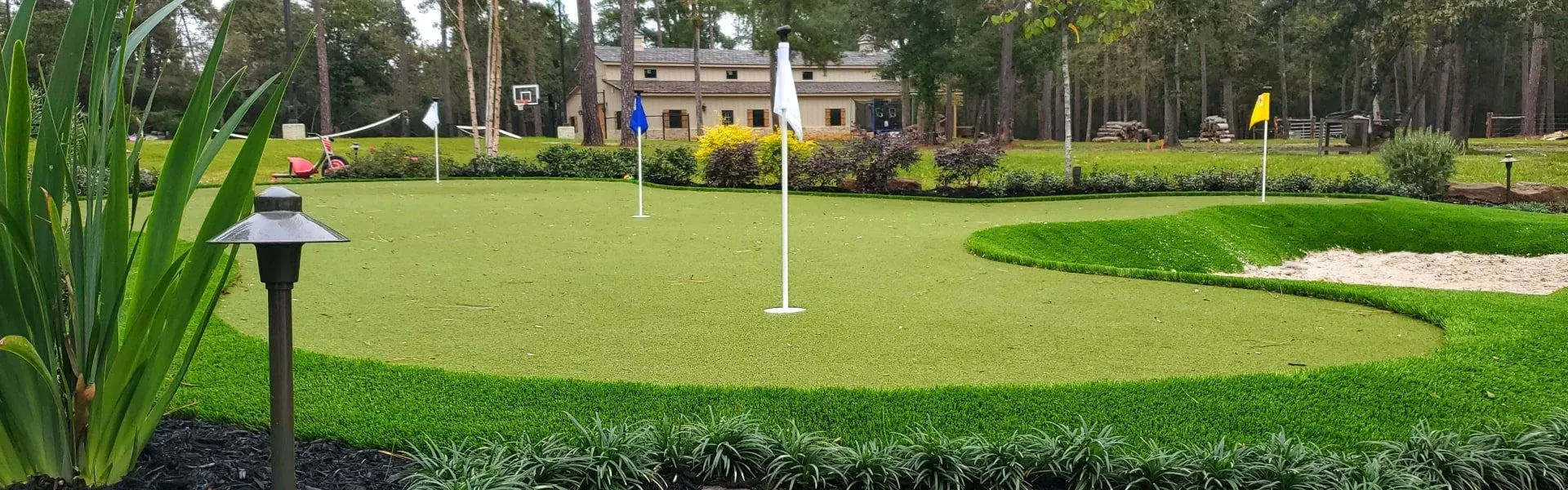 A wide practice green with three flags set into a landscaped lawn